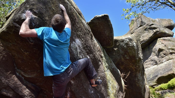 A man reaches up over a rounded rock, while rock climbing at Brimham Rocks, North Yorkshire